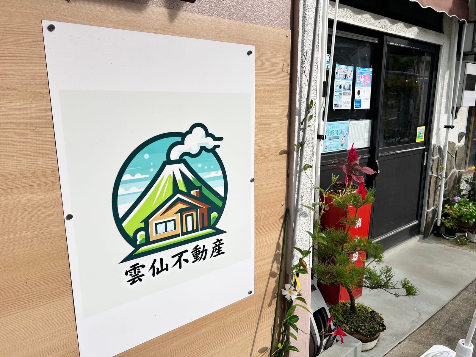 雲仙不動産の事務所入口。雲仙岳と家をかたどったロゴの看板が掲げられている